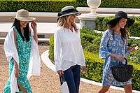 three women wearing sun hats and walking in a garden